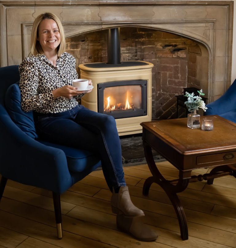 Rachel Brown smiling whilst sitting on an armchair by a fireplace